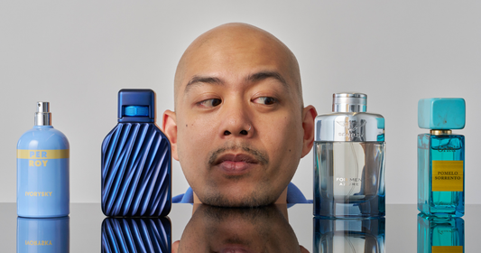 A man is looking at a line up of blue colored perfumes and colognes.