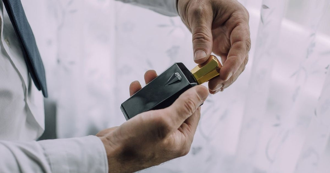 A man holds a dark bottle of cologne with a gold top in his hands.
