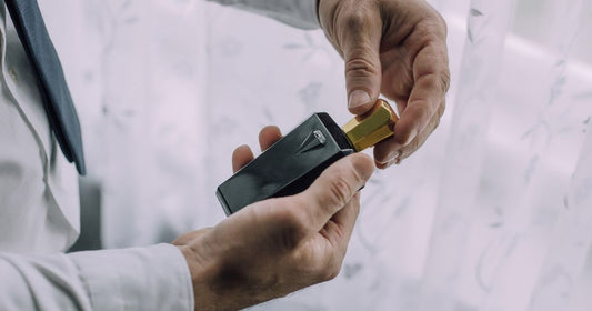 A man holds a dark bottle of cologne with a gold top in his hands.