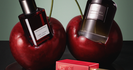Two perfume bottles embedded in two large cherries with a bottle laying on it's side on the ground.