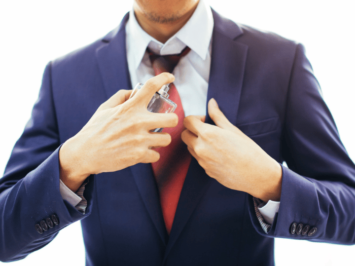 A man wearing a suit sprays cologne on his shirt.