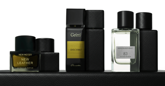 Leather fragrances by Gritti, Banana Republic, and New Notes on a leather table top against a white background.