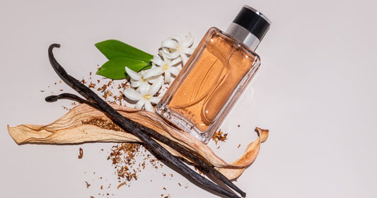 A bottle of vanilla scent on a white background next to a vanilla bean, flowers, and stick.
