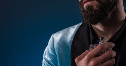 A man wearing a blue jacket spraying a top fragrance for men on his neck.