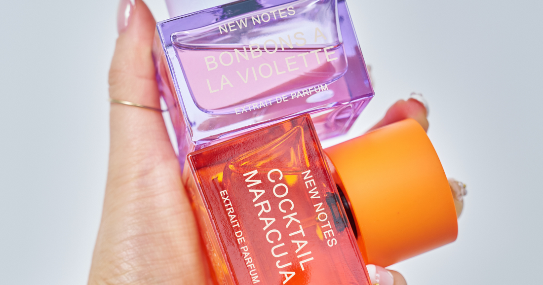 A woman's hand holding a bottle of NEW NOTES  Cocktail Maracuja Extrait de Parfum and Bonbons A La Violette Extrait de Parfum.